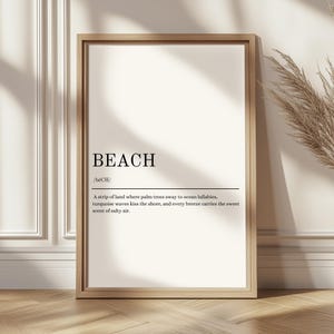 Könnte beinhalten: Ein gerahmter Druck mit dem Wort "BEACH" in fetter Schrift. Darunter beschreibt eine Definition einen Strand als einen Landstreifen, wo Palmen wiegen, türkisfarbene Wellen die Küste küssen und die Brise den Duft salziger Luft trägt. Der Rahmen ist hellbraun.
