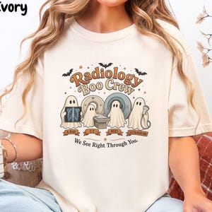 May include: An ivory t-shirt featuring a graphic of four ghosts with medical equipment and the text Radiology Boo Crew and We See Right Through You. The design includes illustrations of an X-ray, CT scanner, MRI machine, and ultrasound probe.