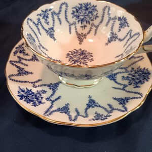 Peut inclure: Une tasse &agrave; th&eacute; et une soucoupe blanches avec un motif floral bleu et or. La tasse et la soucoupe ont un bord festonn&eacute;.