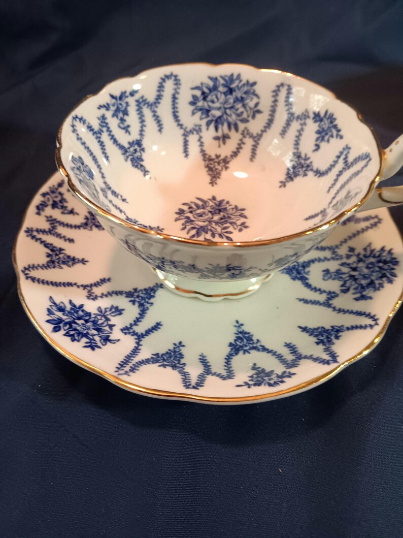 Peut inclure: Une tasse &agrave; th&eacute; et une soucoupe blanches avec un motif floral bleu et or. La tasse et la soucoupe ont un bord festonn&eacute;.