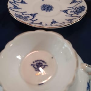 Peut inclure: Une tasse &agrave; th&eacute; et une soucoupe blanches avec un motif floral bleu et blanc. La soucoupe a un bord dor&eacute;. La tasse &agrave; th&eacute; a une marque bleue et blanche au fond qui indique "Colclough" avec une couronne et les mots "Fine Bone China" en cercle.