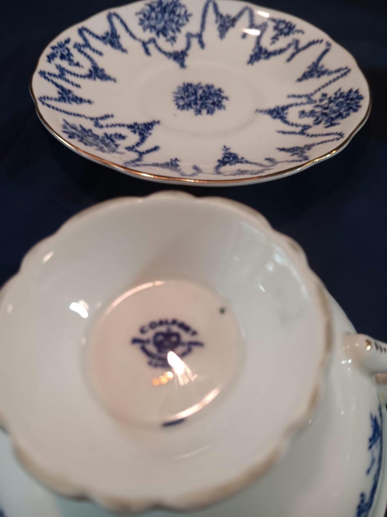 Peut inclure: Une tasse &agrave; th&eacute; et une soucoupe blanches avec un motif floral bleu et blanc. La soucoupe a un bord dor&eacute;. La tasse &agrave; th&eacute; a une marque bleue et blanche au fond qui indique "Colclough" avec une couronne et les mots "Fine Bone China" en cercle.
