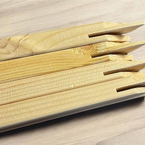 A stack of light-colored wooden stretcher bar pieces with notched ends is shown on a light wood-grain surface.
