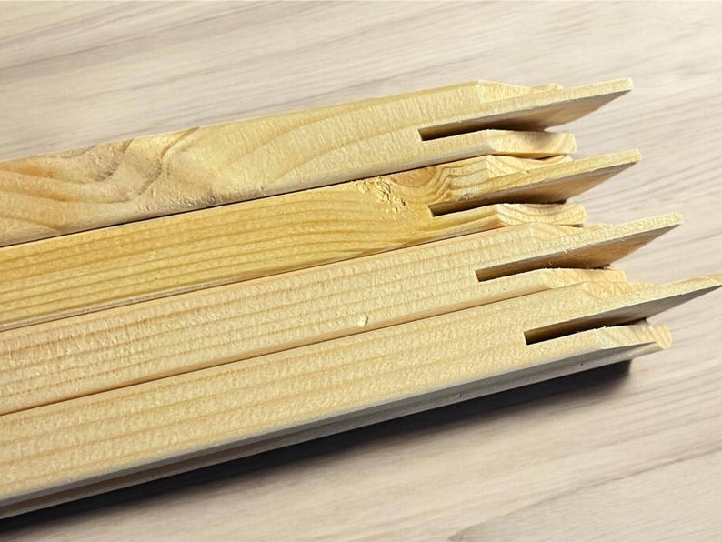 A stack of light-colored wooden stretcher bar pieces with notched ends is shown on a light wood-grain surface.