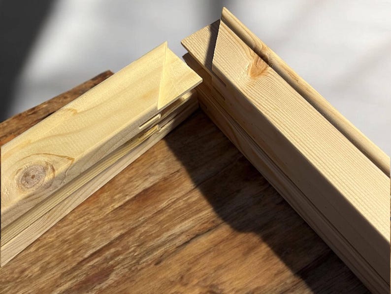 A close-up shows two light-colored wooden stretcher bar pieces joined at a corner, resting on a dark wood surface.