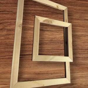 Two light-colored wooden stretcher bar frames, one large and one small, are arranged on a dark wood-grain surface.