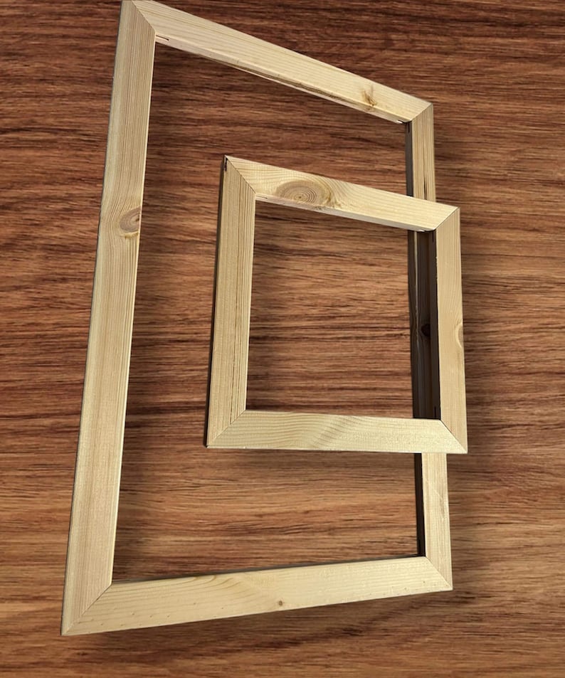 Two light-colored wooden stretcher bar frames, one large and one small, are arranged on a dark wood-grain surface.