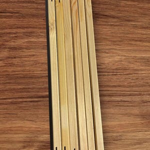 A stack of light-colored wooden stretcher bar pieces with notched ends is laid flat on a dark wood-grain surface.