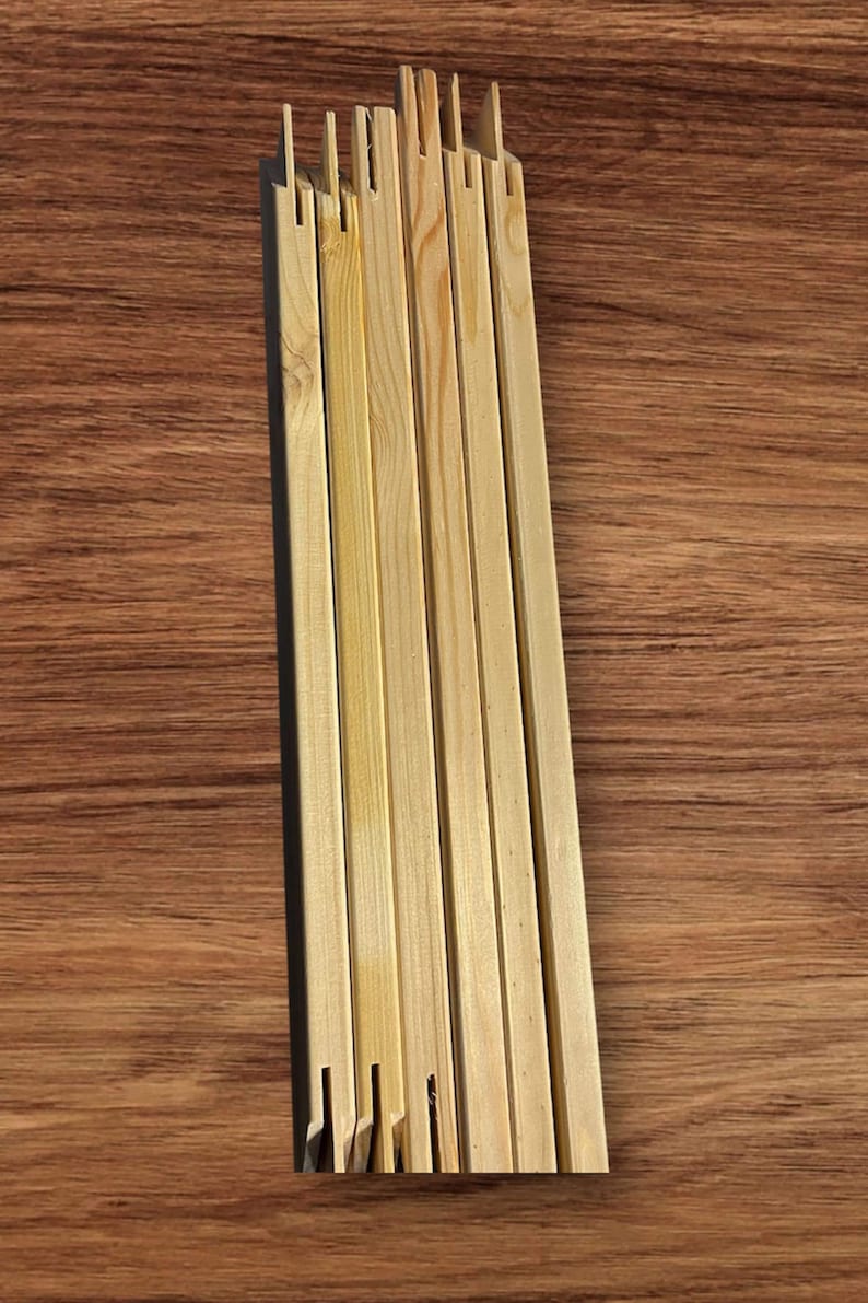 A stack of light-colored wooden stretcher bar pieces with notched ends is laid flat on a dark wood-grain surface.