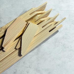 A pile of light-colored wooden stretcher bar pieces with various notches and a few small wooden wedges are shown on a light gray surface.