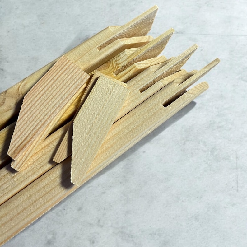 A pile of light-colored wooden stretcher bar pieces with various notches and a few small wooden wedges are shown on a light gray surface.