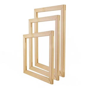 Three light-colored wooden stretcher bar frames of varying sizes are stacked and leaning against a white background.