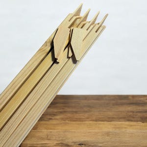 A bundle of light-colored wooden stretcher bar pieces with notched ends and several small wooden wedges are leaning against a white background, with a dark wood surface in the foreground.