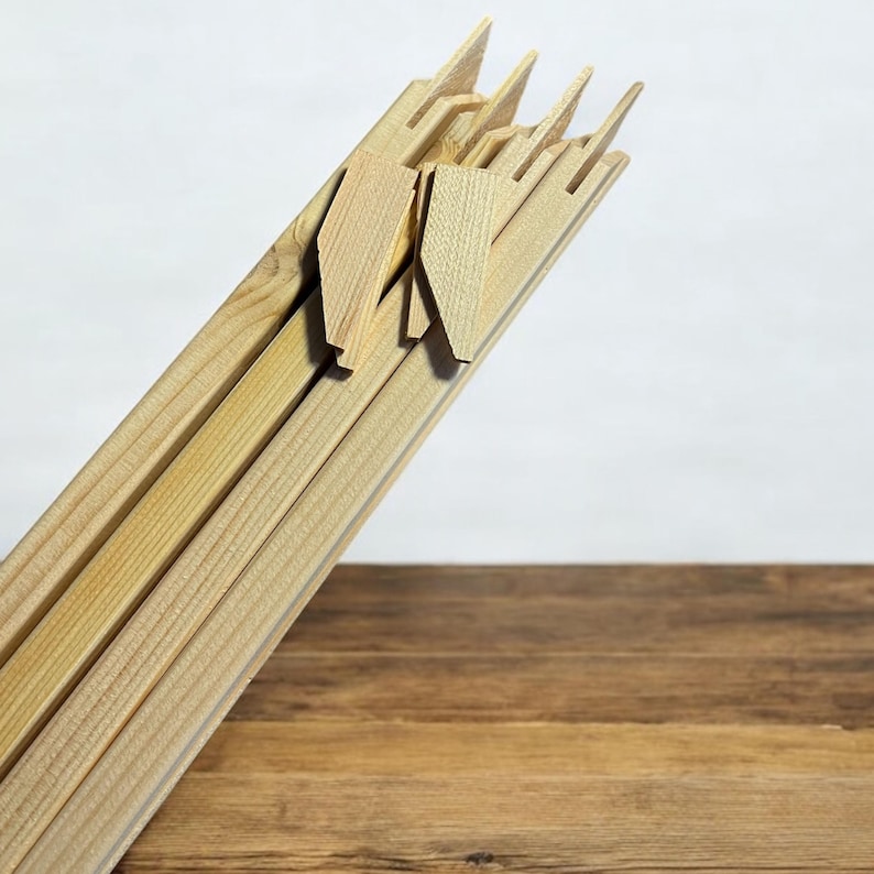 A bundle of light-colored wooden stretcher bar pieces with notched ends and several small wooden wedges are leaning against a white background, with a dark wood surface in the foreground.