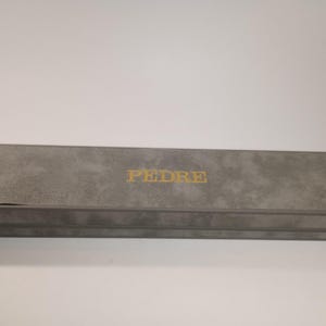 May include: A gray rectangular box with the word "PEDRE" printed in gold lettering on the top.