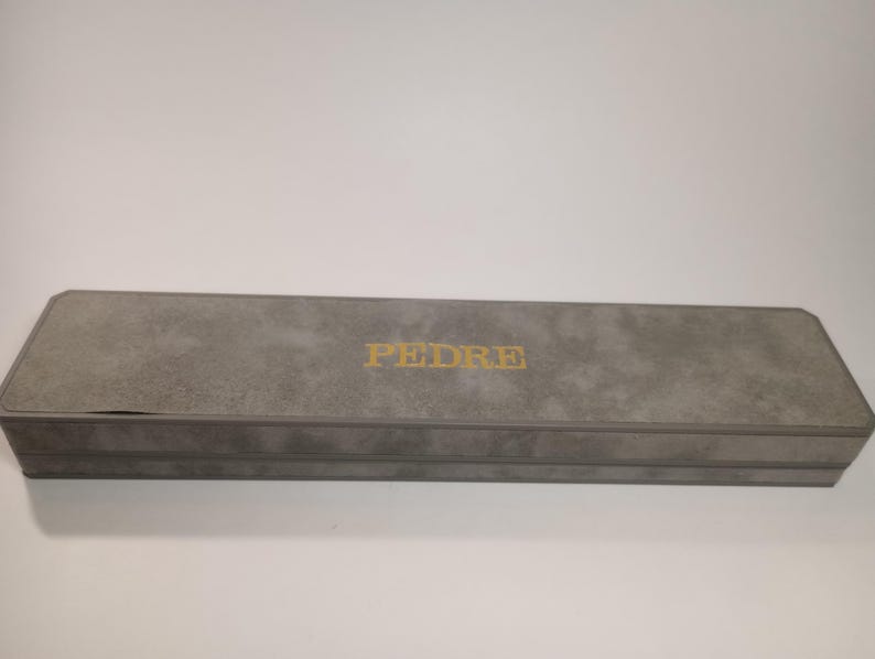 May include: A gray rectangular box with the word "PEDRE" printed in gold lettering on the top.