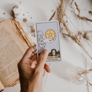 May include: A tarot card with a hand holding a pentagram inside a circle. The card is called "Ten of Pentacles".