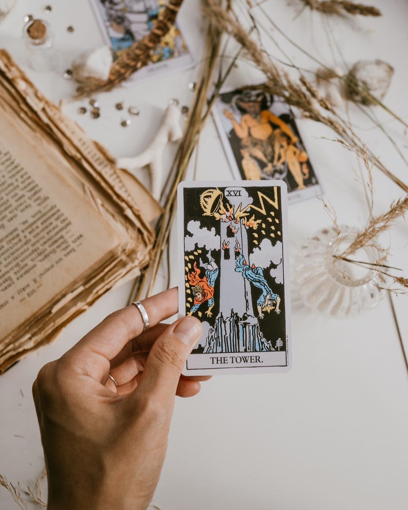 May include: A tarot card with the image of a tower being struck by lightning. The card is labeled "XVI THE TOWER".