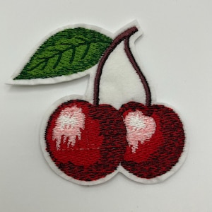 Könnte beinhalten: Ein gestickter Kirsch-Patch mit einem grünen Blatt. Die Kirsche ist eine beliebte Frucht und wird oft als Symbol für Liebe und Glück verwendet.