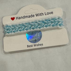 May include: A white card with the text "Handmade With Love" and a red heart. The card has a blue and white rubber band on top of it. The card also has a holographic sticker that says "Thank You for supporting my small business" with a red heart. The card also has the text "Best Wishes" on it.