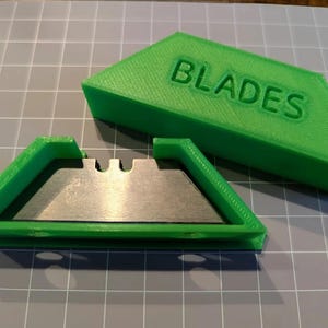 May include: A green plastic case with the word "BLADES" printed on the top. The case is open and a silver razor blade is visible inside.