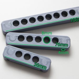 Puede incluir: Tres objetos grises rectangulares impresos en 3D con agujeros circulares. El más grande mide 10,6 cm de largo, el del medio 7,6 cm y el más pequeño 5,6 cm. Cada uno tiene una serie de agujeros espaciados.