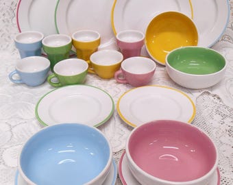 May include: A collection of colorful ceramic dishware, including plates, bowls, and cups. The plates have colored rims in pink, green, yellow, and blue. The cups and bowls are in matching colors, creating a vibrant and coordinated set.