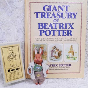 May include: A collection of Beatrix Potter books and a small bunny figurine. The large book is titled "Giant Treasury of Beatrix Potter." The bunny figurine is wearing a coat and holding a miniature book.