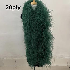 Pode incluir: Uma longa boa de penas verde esmeralda exibida em um manequim. A boa é feita de penas macias e fofas e é drapeada ao redor do pescoço do manequim. O texto "20ply" é visível no canto superior esquerdo.