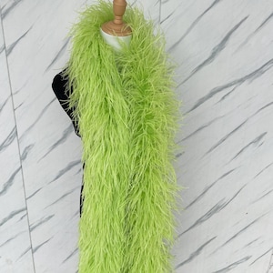 May include: A long, vibrant lime green feather boa draped over a mannequin. The accessory is composed of numerous thin, wispy feathers that create a dense, textured appearance, providing a full and voluminous look across the entire length.
