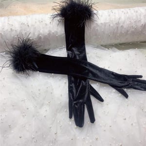May include: A pair of elegant black velvet opera gloves with feather trim at the wrist. The gloves are long, extending past the elbow, and are displayed against a white, textured background.