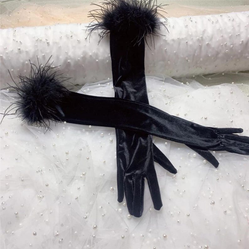 May include: A pair of elegant black velvet opera gloves with feather trim at the wrist. The gloves are long, extending past the elbow, and are displayed against a white, textured background.