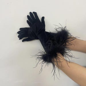 May include: A pair of black velvet gloves with long sleeves. The cuffs are adorned with black feathers. The gloves are displayed against a plain white background.