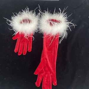 May include: A pair of red velvet gloves, one long and one short, with white feather trim around the wrist. The gloves are displayed on a black surface. The long glove is approximately 18 inches long.