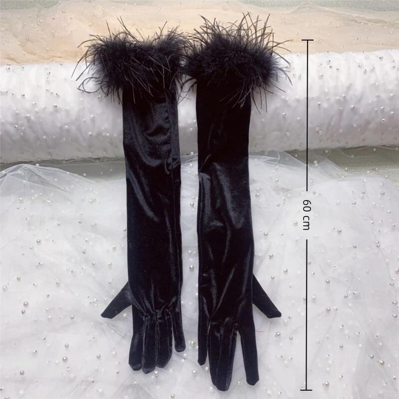 May include: A pair of long, black velvet gloves with a feather trim at the wrist. The gloves measure approximately 23.6 inches (60 cm) in length. The gloves are displayed on a white surface.