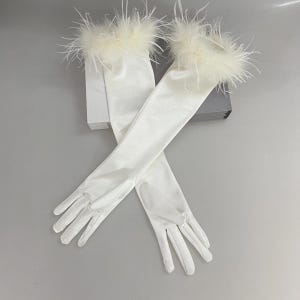 May include: A pair of elegant, white satin gloves with long sleeves. The cuffs are trimmed with fluffy, cream-colored feathers. The gloves are laid out on a light gray surface.