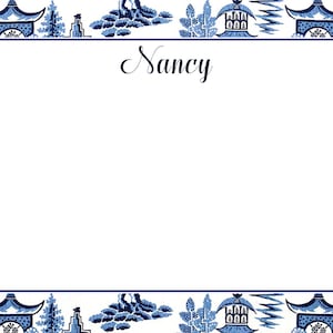 May include: A white card with a blue and white border featuring a traditional Chinese pattern. The card has a white space in the center with the name "Nancy" written in cursive.