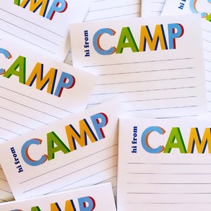 May include: A stack of white lined notepads with the word "CAMP" printed in colorful, layered letters on each notepad. The text "hi from" is printed on each notepad.