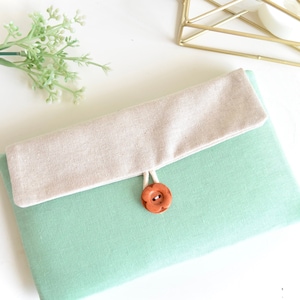 May include: A light green fabric pouch with a beige flap and a brown button closure.