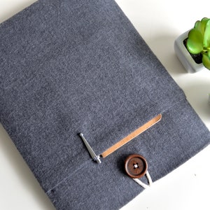 Peut inclure: Une housse pour ordinateur portable en tissu gris &agrave; chevrons avec un rabat en cuir marron et une fermeture &agrave; bouton en bois. La housse a une petite poche sur le devant.
