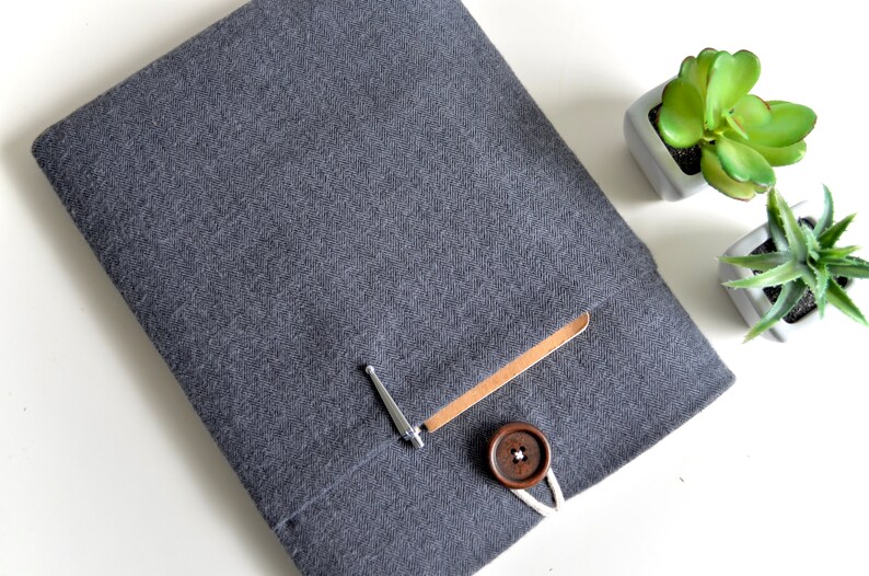 Peut inclure: Une housse pour ordinateur portable en tissu gris &agrave; chevrons avec un rabat en cuir marron et une fermeture &agrave; bouton en bois. La housse a une petite poche sur le devant.