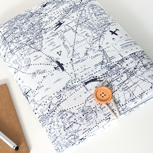 May include: A white laptop sleeve with a blue and white world map print. The sleeve has a brown button closure and a white fabric strap. The text "Around the World" is printed on the sleeve.