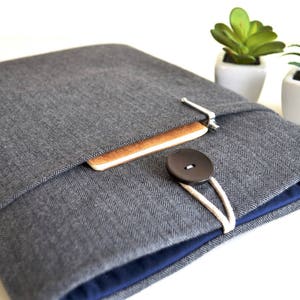 May include: A gray herringbone fabric laptop sleeve with a blue lining, a brown notebook inside, and a black button closure.