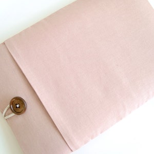 May include: A blush pink fabric laptop sleeve with a wooden button closure.