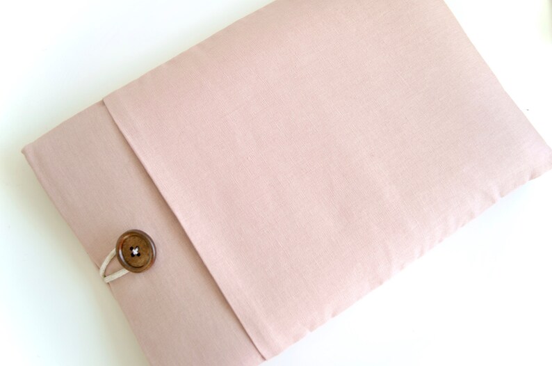 May include: A blush pink fabric laptop sleeve with a wooden button closure.