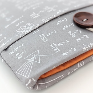 May include: Gray fabric laptop sleeve with a white print of mathematical formulas and symbols. The sleeve has a brown button closure and an orange lining.