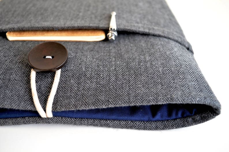 May include: A gray herringbone fabric laptop sleeve with a blue lining and a brown button closure.