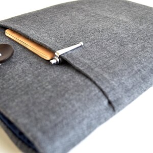 May include: A gray fabric laptop sleeve with a flap closure and a button. The sleeve has a pocket on the front for a notebook and pen.