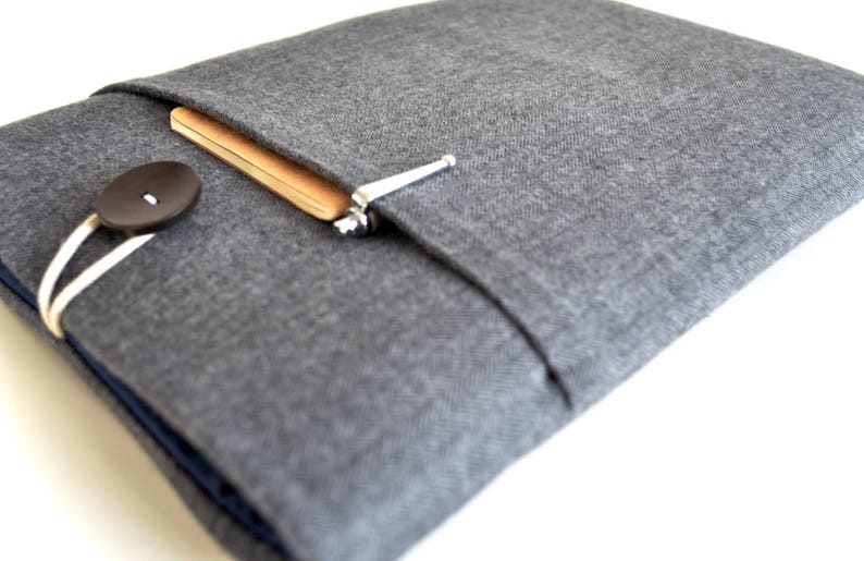 May include: A gray fabric laptop sleeve with a flap closure and a button. The sleeve has a pocket on the front for a notebook and pen.