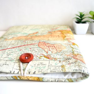 Puede incluir: Una cubierta de cuaderno de tela marrón y blanca con un diseño de mapa del mundo vintage. La cubierta tiene un cierre de botón rojo y una corbata de cuerda blanca.
